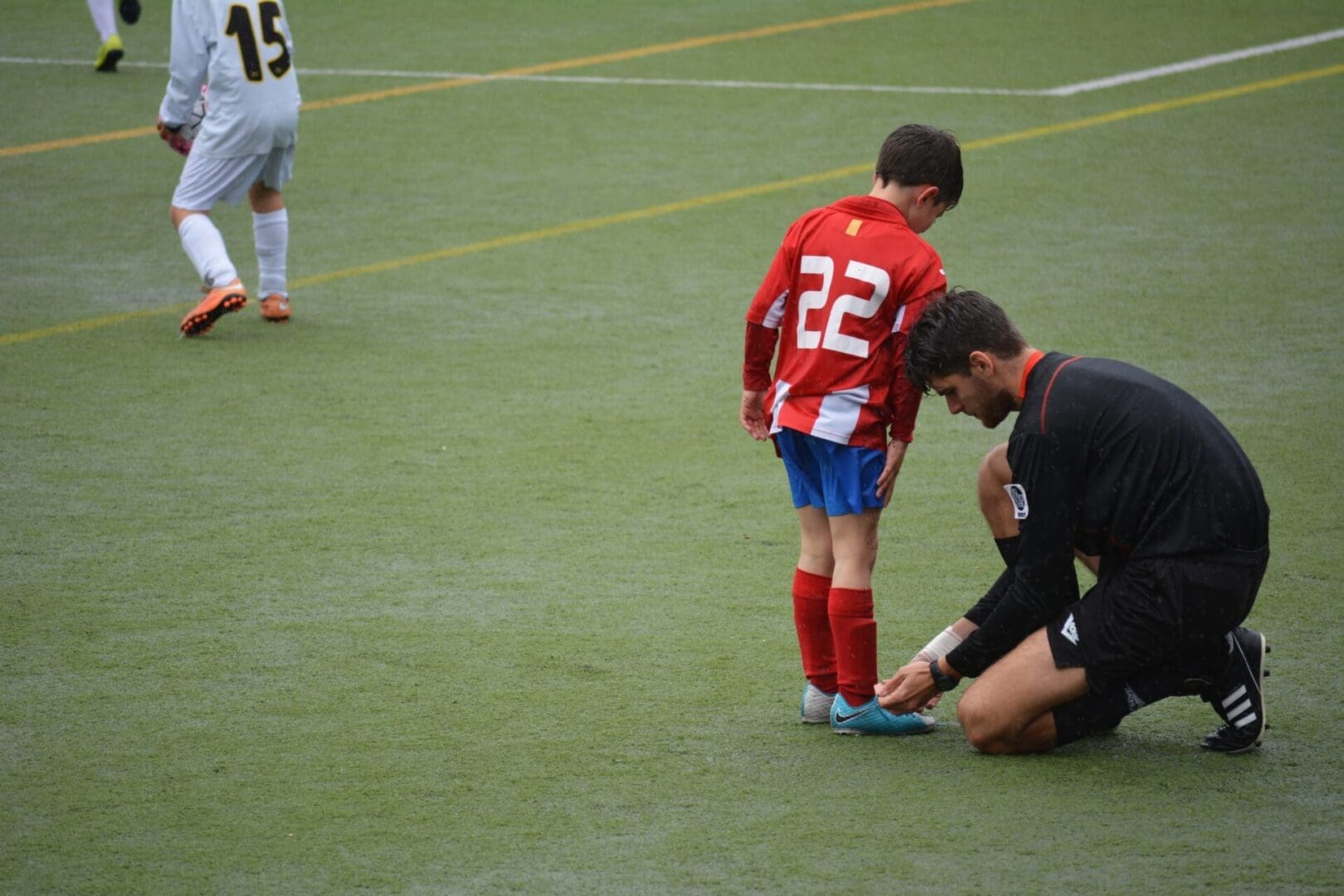 A man helping a young boy put on his soccer shoes.